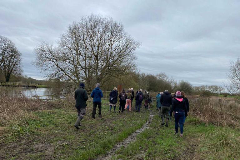 a group of people wearing warm clothing and boots walking alongside a river